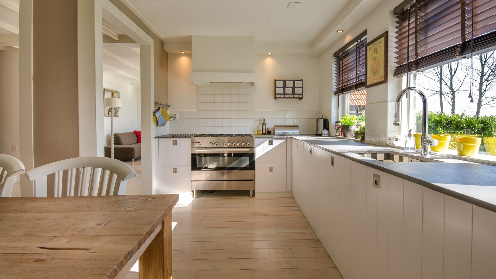 Modern white kitchen with wooden table, stainless steel appliances, and large window