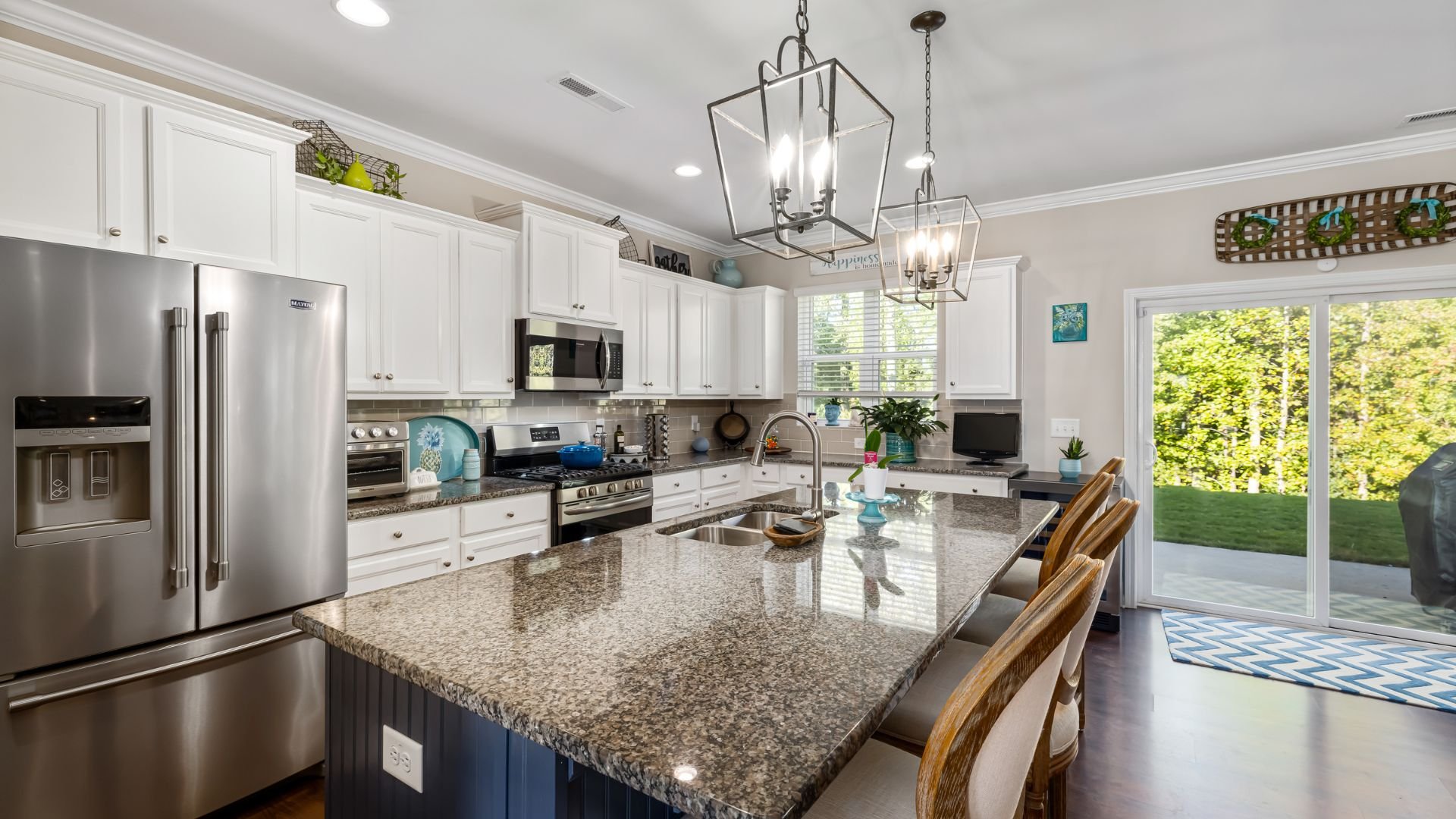 Modern white kitchen with granite island, stainless steel appliances, and garden view