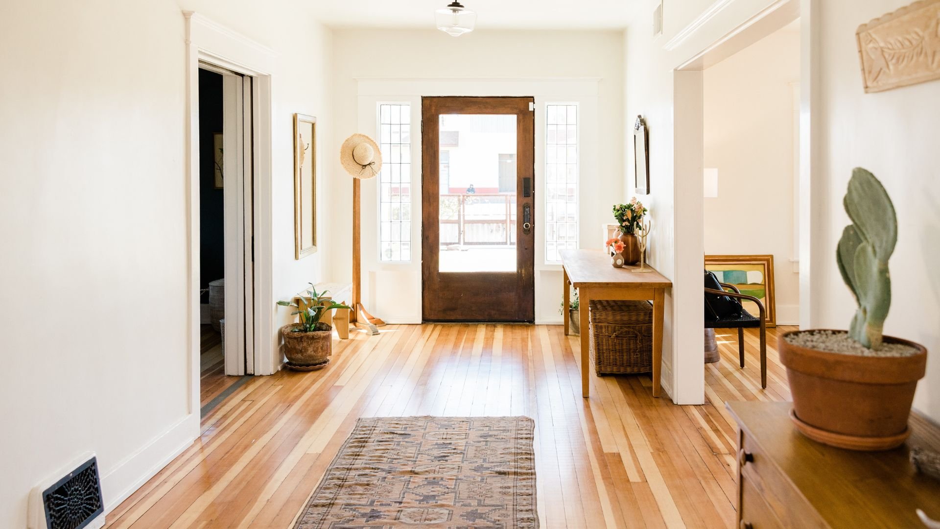 Bright entryway with wooden door, plants, rug, and hardwood floors