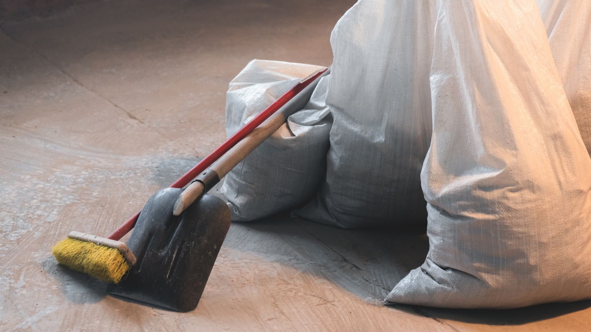 Dustpan, broom, and gray sacks on wooden floor for cleaning