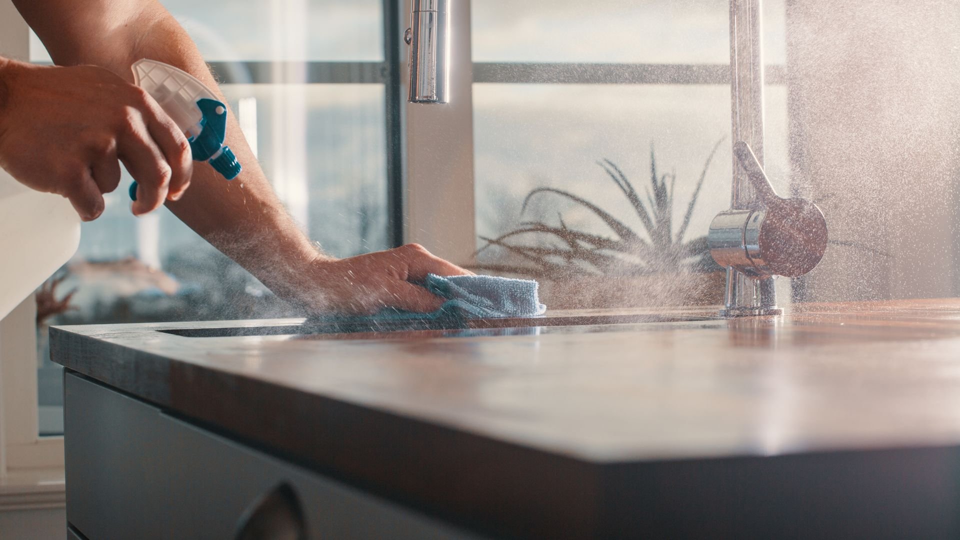 Hands cleaning kitchen counter with spray bottle and microfiber cloth