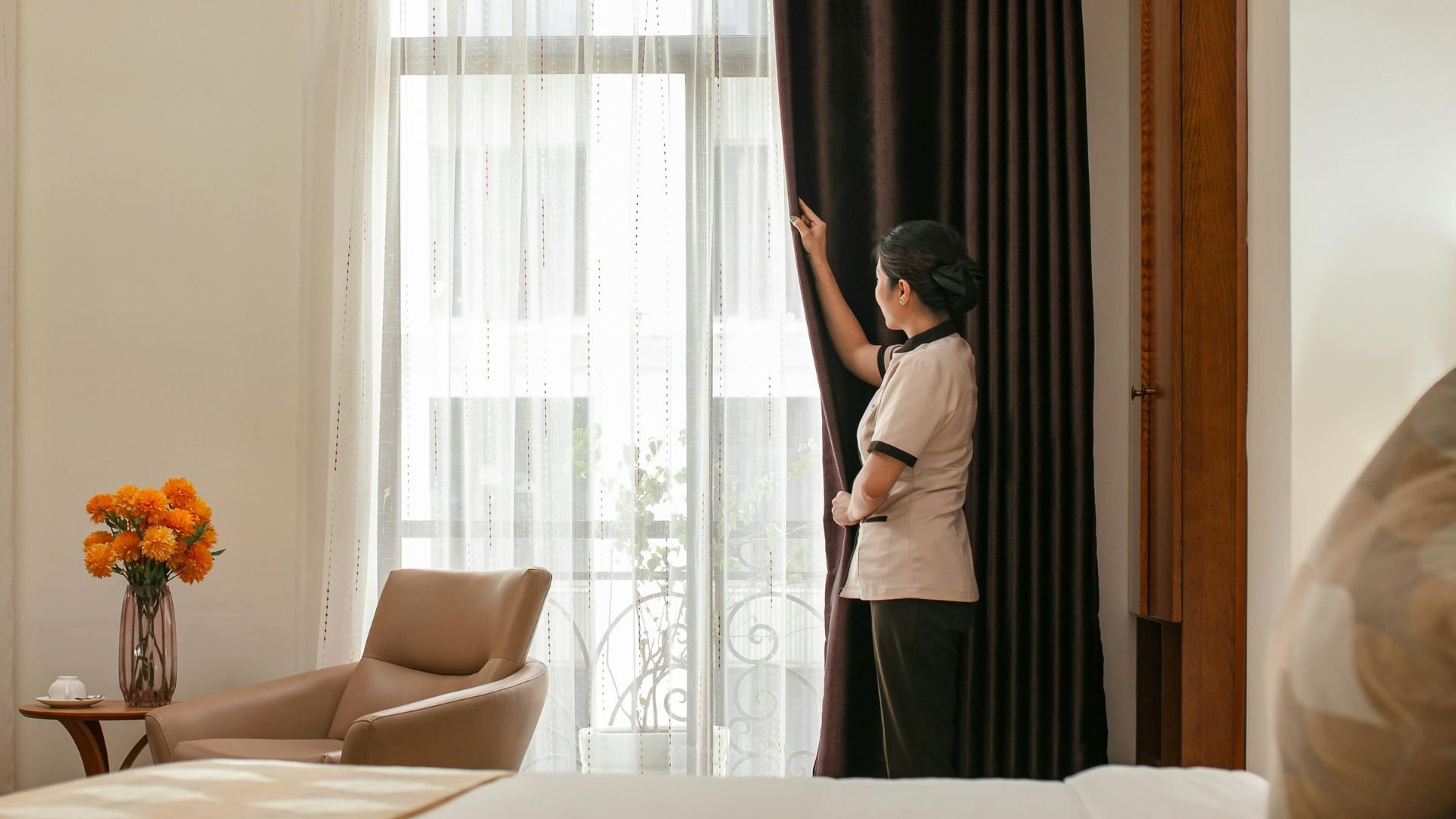 Housekeeper adjusting curtains in a bright, elegant hotel room